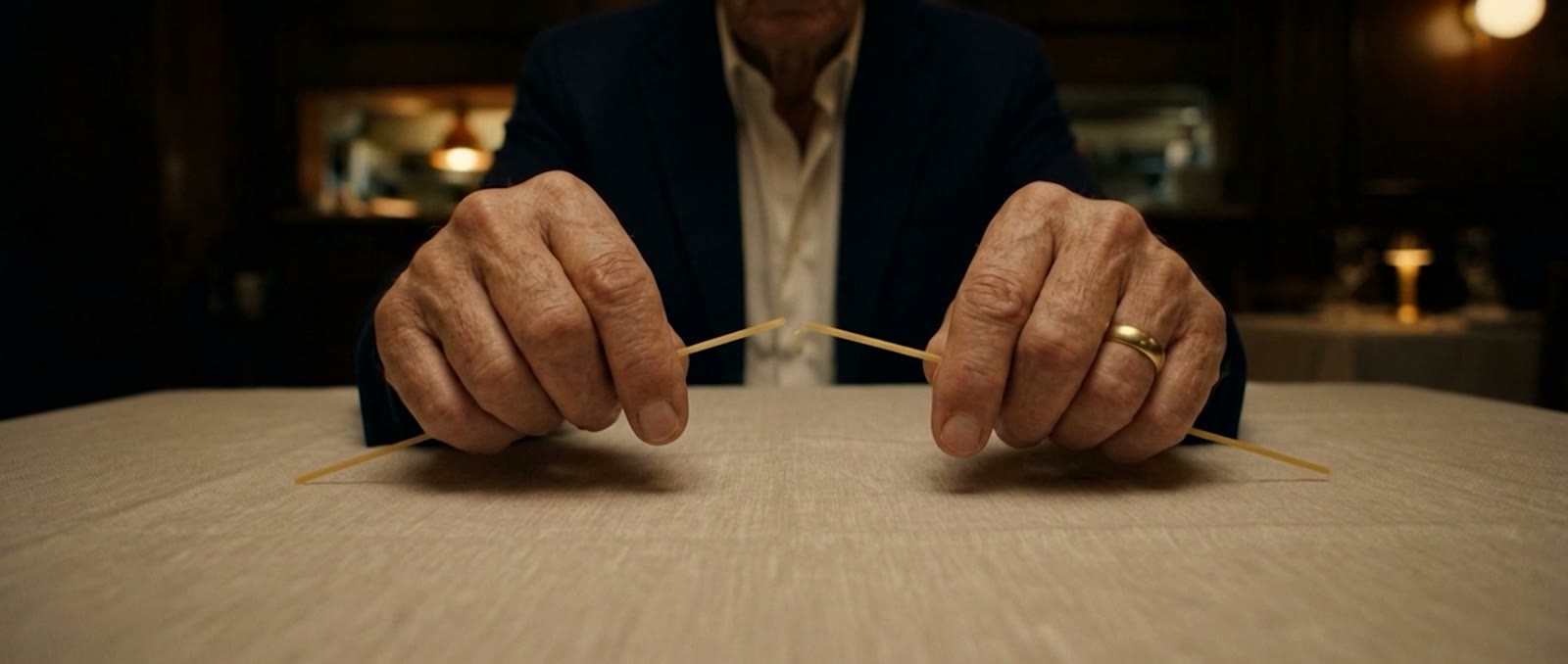 Weathered hands snap a single spaghetti over white linen