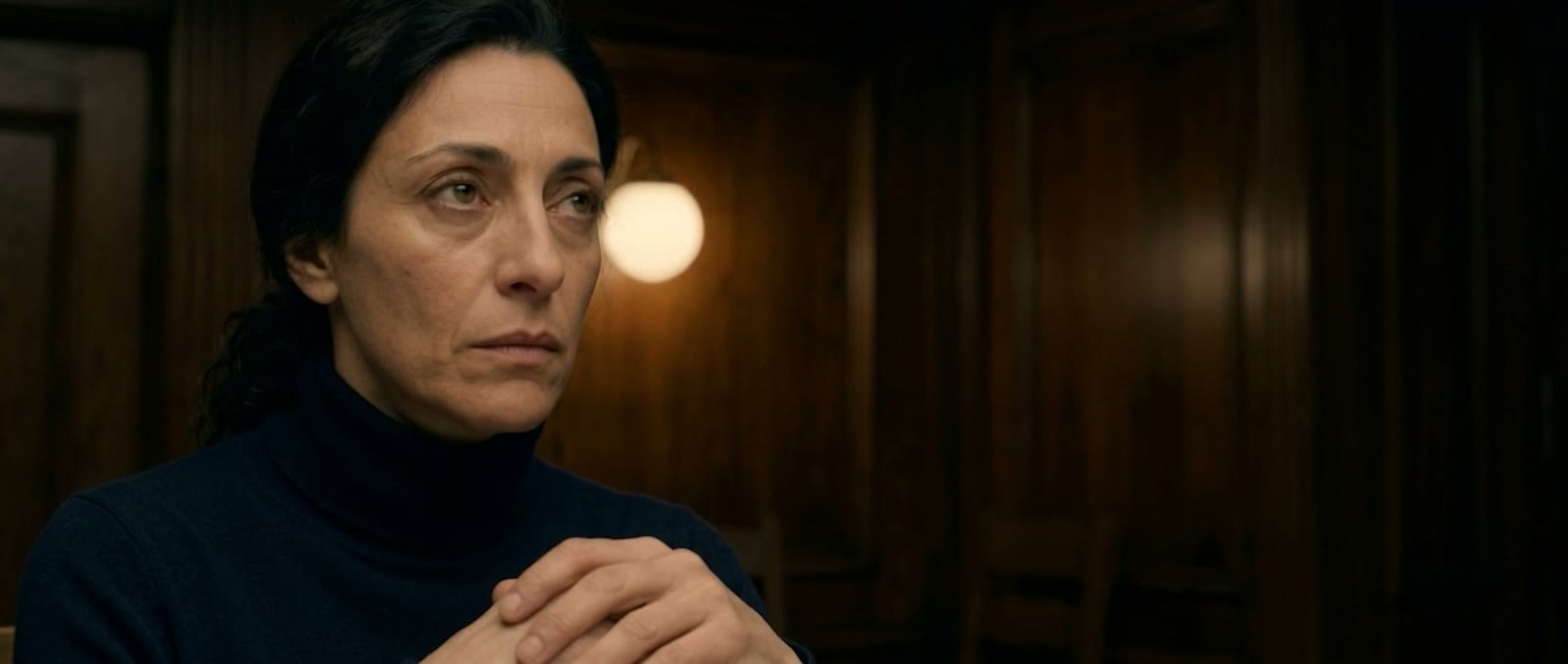 A woman waits in silence, hands clasped, deep in the trattoria