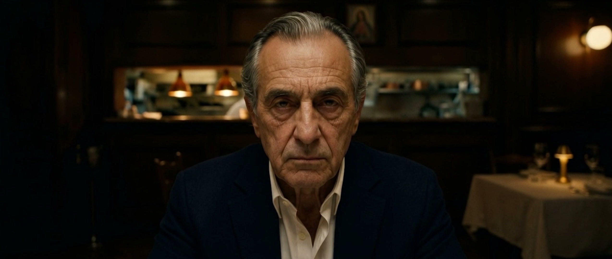 An elderly patriarch stares into camera inside a dark trattoria