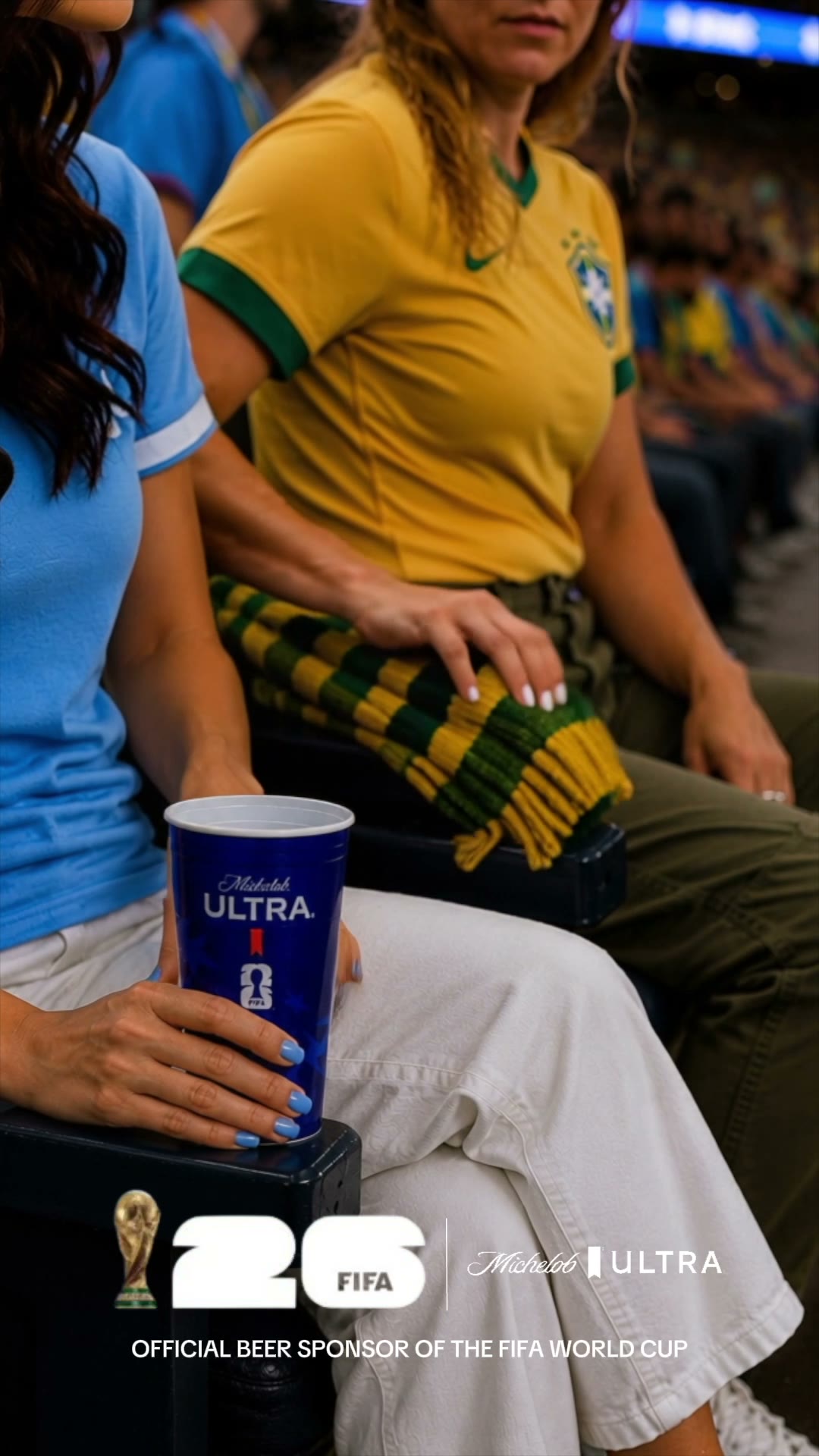 A Uruguay fan and a Brazil fan share a stadium armrest, a Michelob Ultra cup in hand